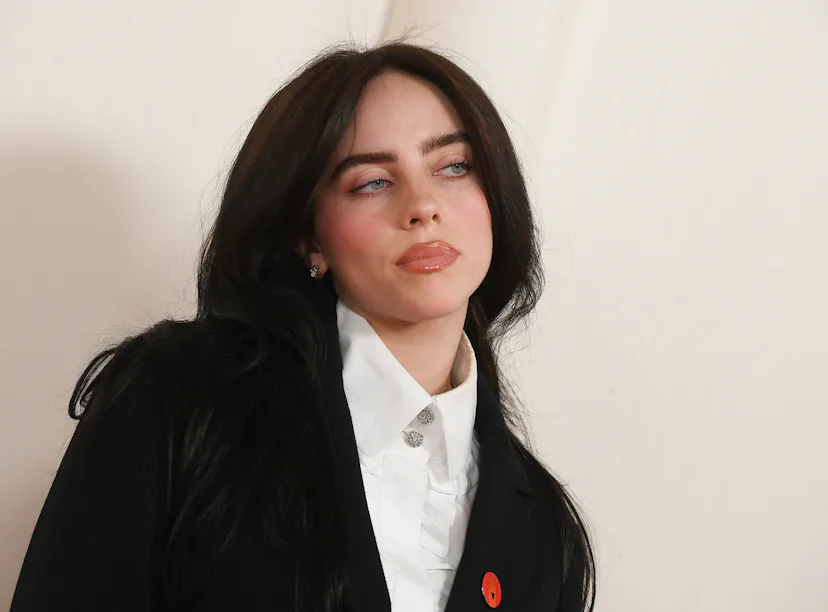 Woman with dark hair in a black coat over a white shirt, looking to her right, slight smile, neutral...