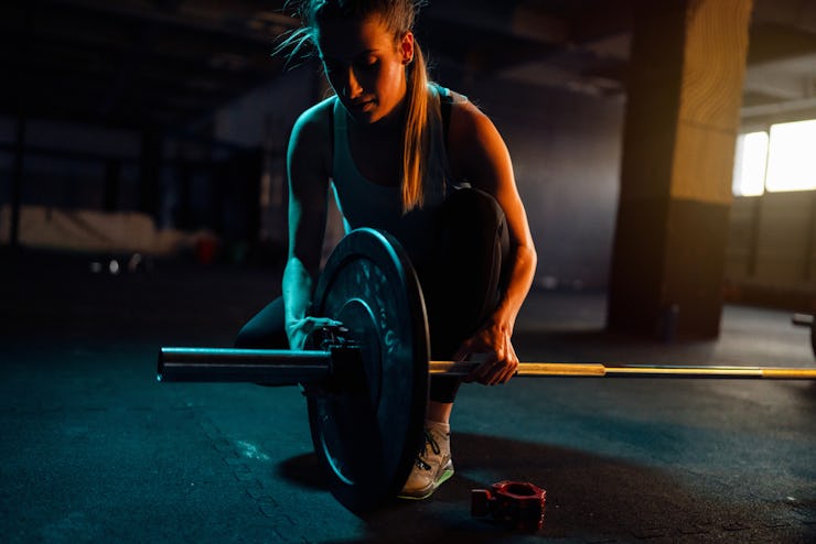 Young Caucasian woman, adjusting weights on a barbell, during workout in the gym