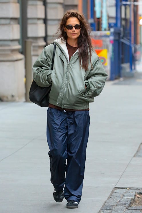 Woman in a green bomber jacket and navy trousers walking on a city street.