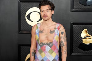 Man in colorful patchwork vest over bare chest, standing in front of a black patterned backdrop at a...