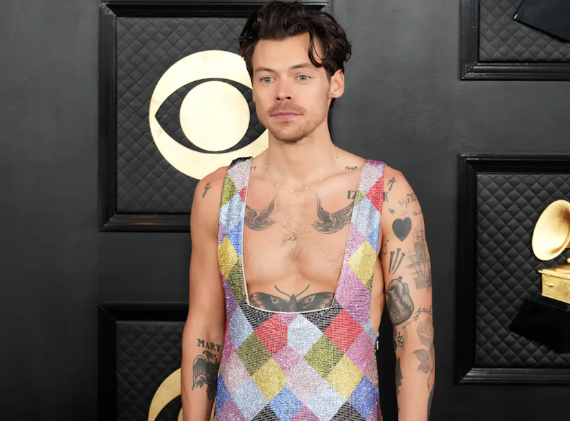 Man in colorful patchwork vest over bare chest, standing in front of a black patterned backdrop at a...