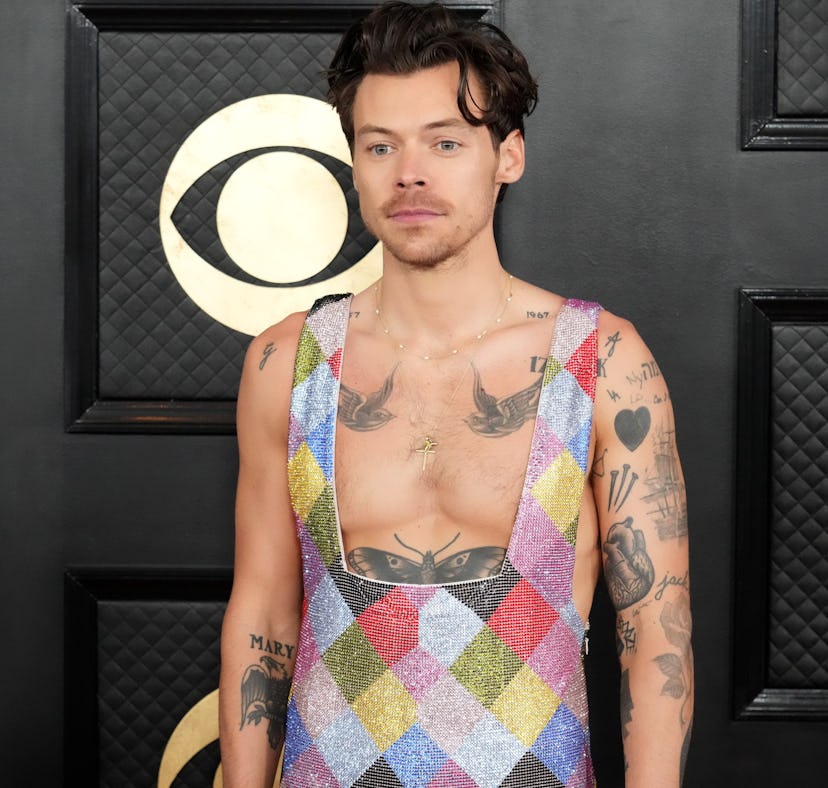 Man in colorful patchwork vest over bare chest, standing in front of a black patterned backdrop at a...