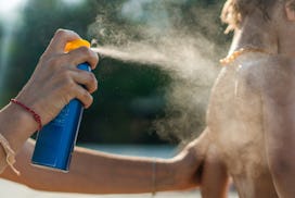 Unrecognizable mother spraying suntan lotion on her son's body at the beach.
