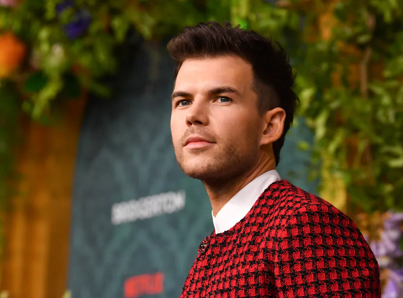 Man in a stylish red and black checked sweater looking away thoughtfully against a vibrant floral ba...