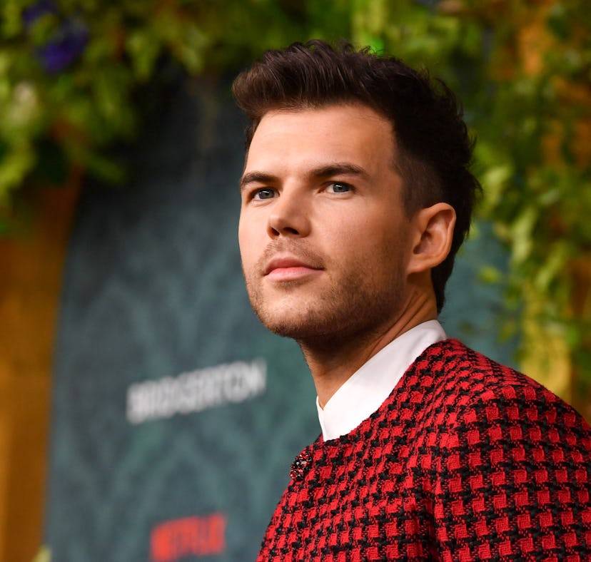 Man in a stylish red and black checked sweater looking away thoughtfully against a vibrant floral ba...