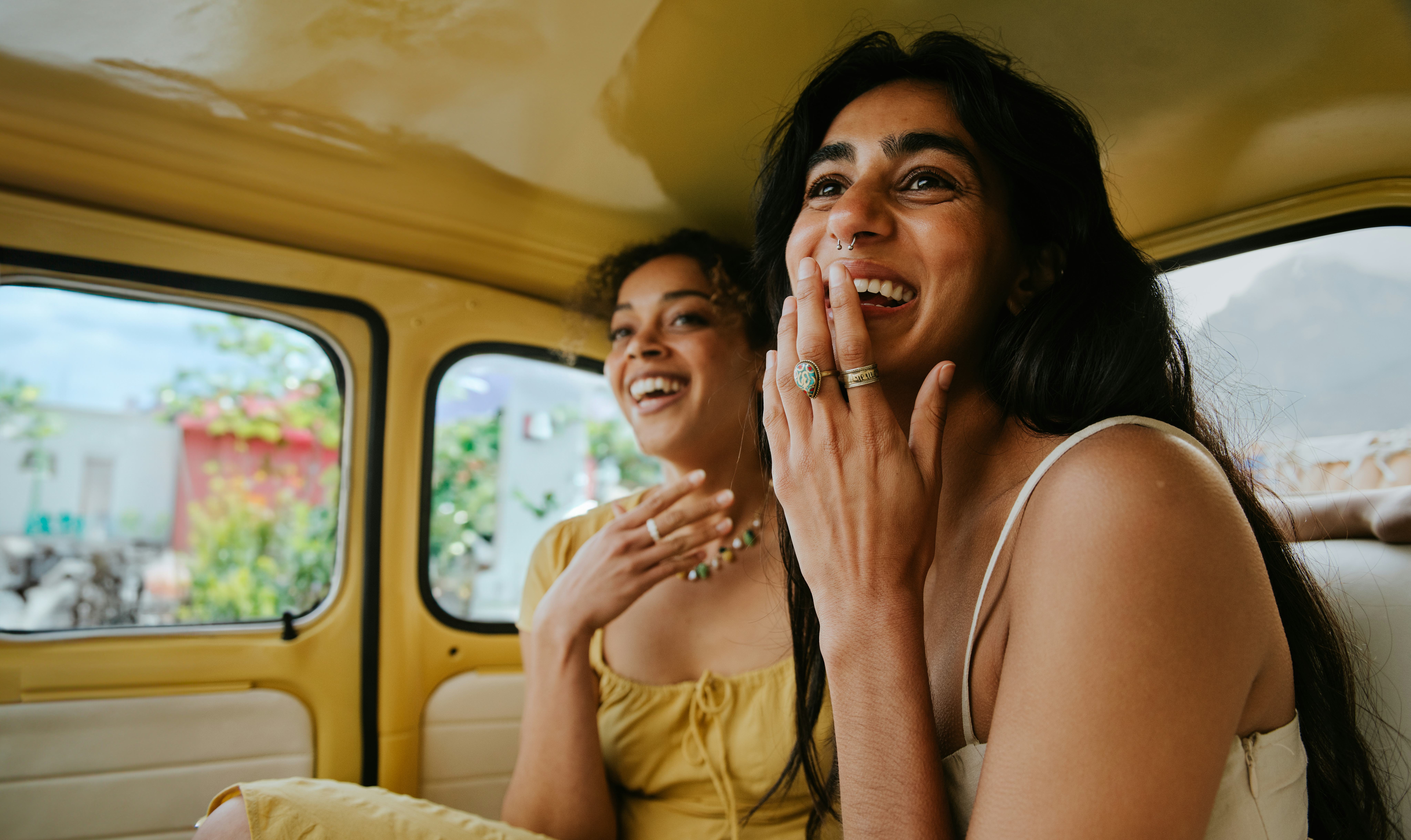 Two woman ask each other juicy Never Have I Ever questions on a road trip in a car