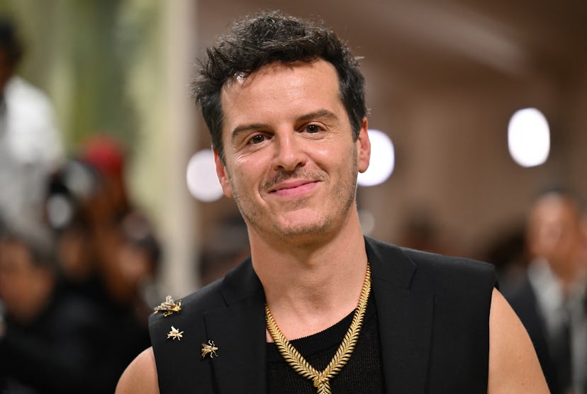 Man with a confident smile wearing a black sleeveless top adorned with star pins and multiple neckla...