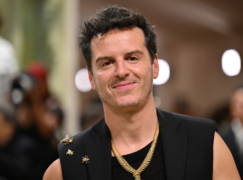 Man with a confident smile wearing a black sleeveless top adorned with star pins and multiple neckla...