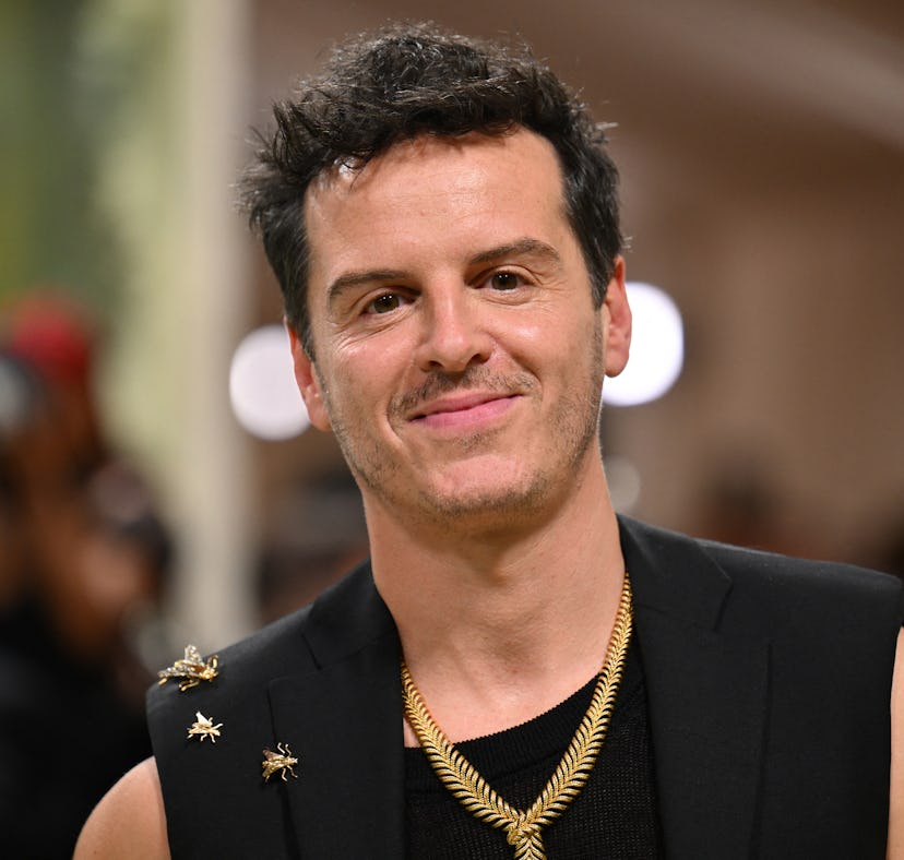 Man with a confident smile wearing a black sleeveless top adorned with star pins and multiple neckla...