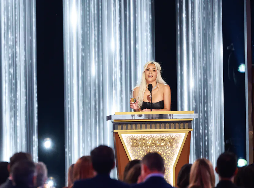A woman speaks at a podium on a stage adorned with vertical light strands, addressing an audience at...