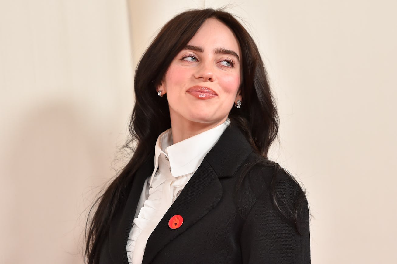 Woman in a black blazer and white shirt with a red poppy pin, smiling and looking away.