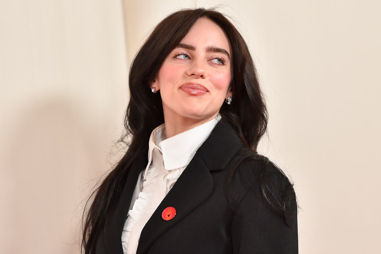 Woman in a black blazer and white shirt with a red poppy pin, smiling and looking away.