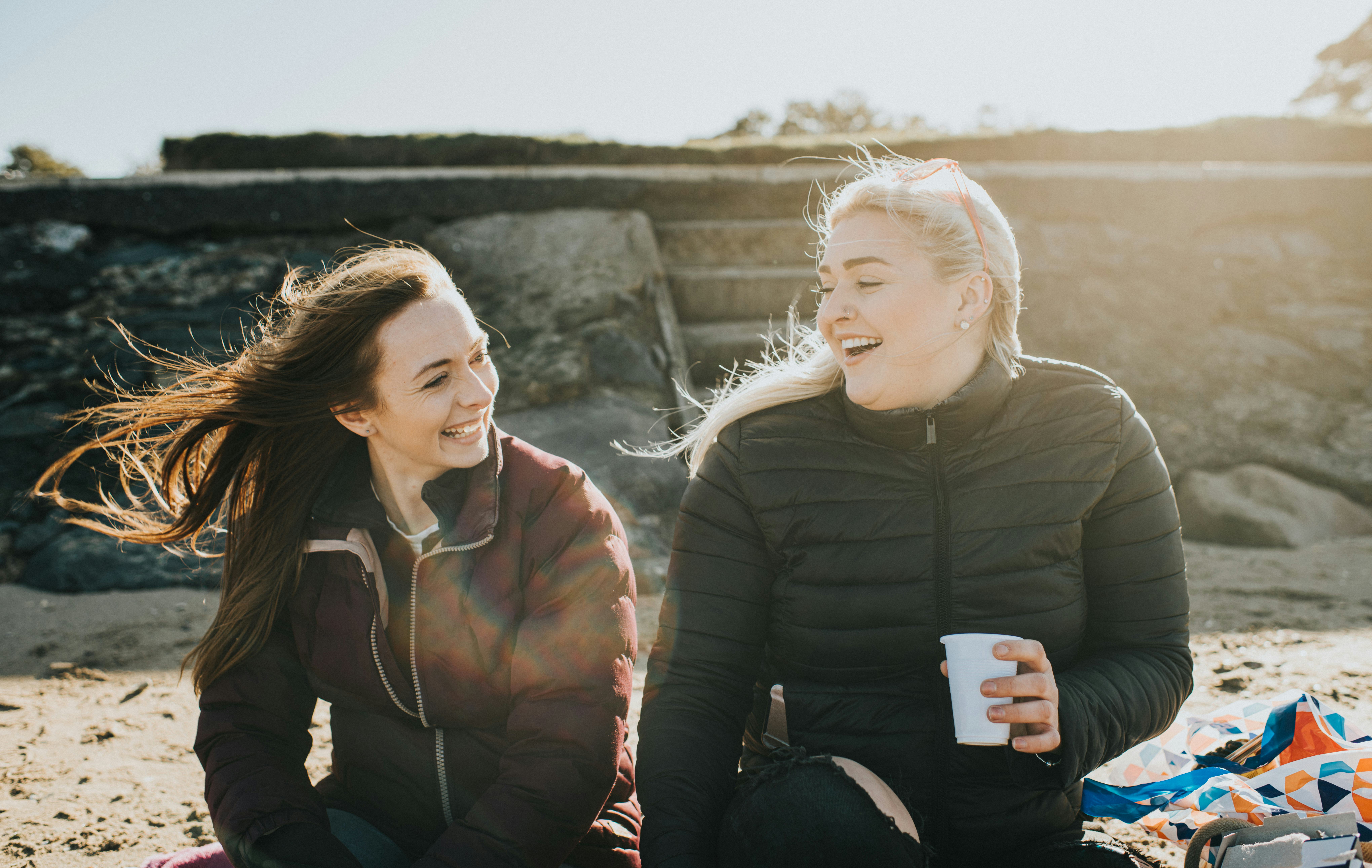 Two young woman sit on a beach and ask each other Never Have I Ever questions