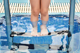 little girl by the side of an outdoor swimming pool, dipping her toes in the water.