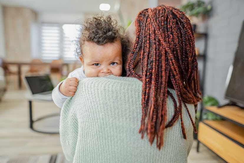 Black mother holding her baby son over shoulder at home