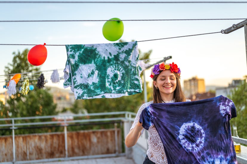 Young cheerful girl hanging a freshly made tie-dye t-shirt on a rope on the terrace.