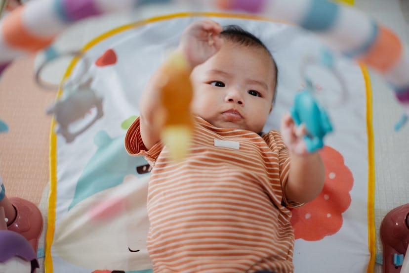 Asian cute baby boy playing hanging toys on baby gymnasium at home