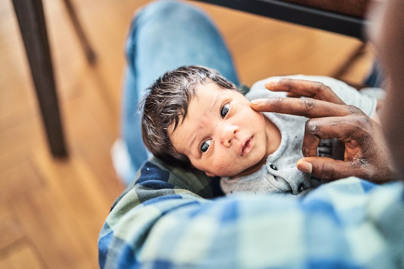 High angle view of cute newborn in father's arms at home. Close-up of a man holding son in living ro...