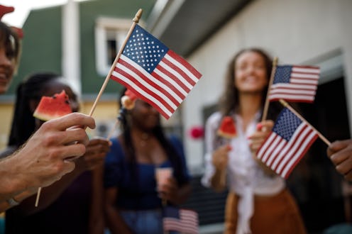 Candid shot of diverse group of joyful young people, friends, having fun, dancing and waving America...