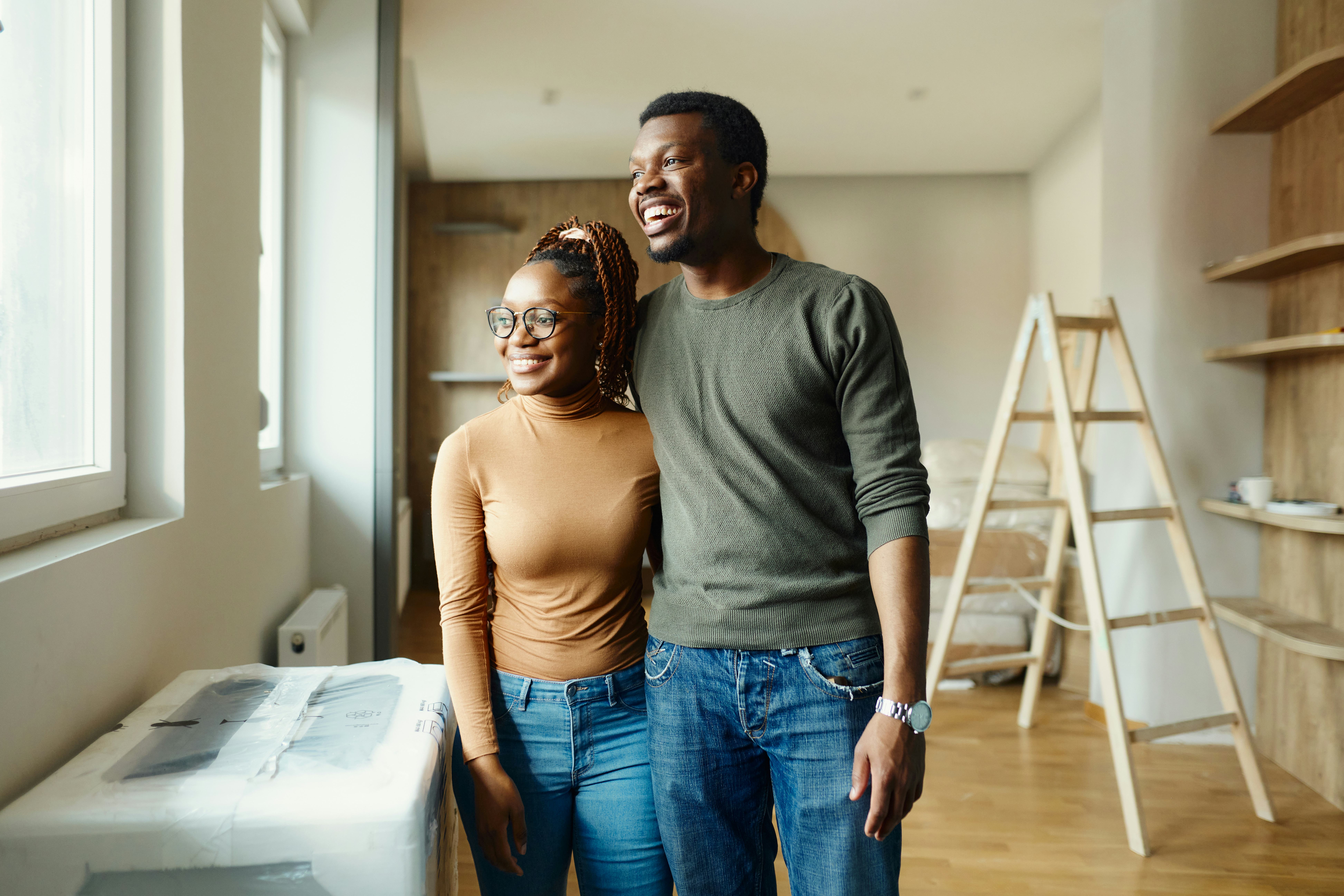 Happy couple looking through window in their new home and laughing at good house and home jokes.