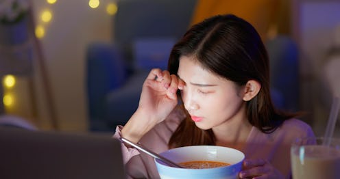 asian woman feeling pain in dry eye strain is eating instant noodles and tapioca ball milk while wor...