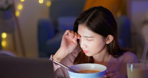 asian woman feeling pain in dry eye strain is eating instant noodles and tapioca ball milk while wor...