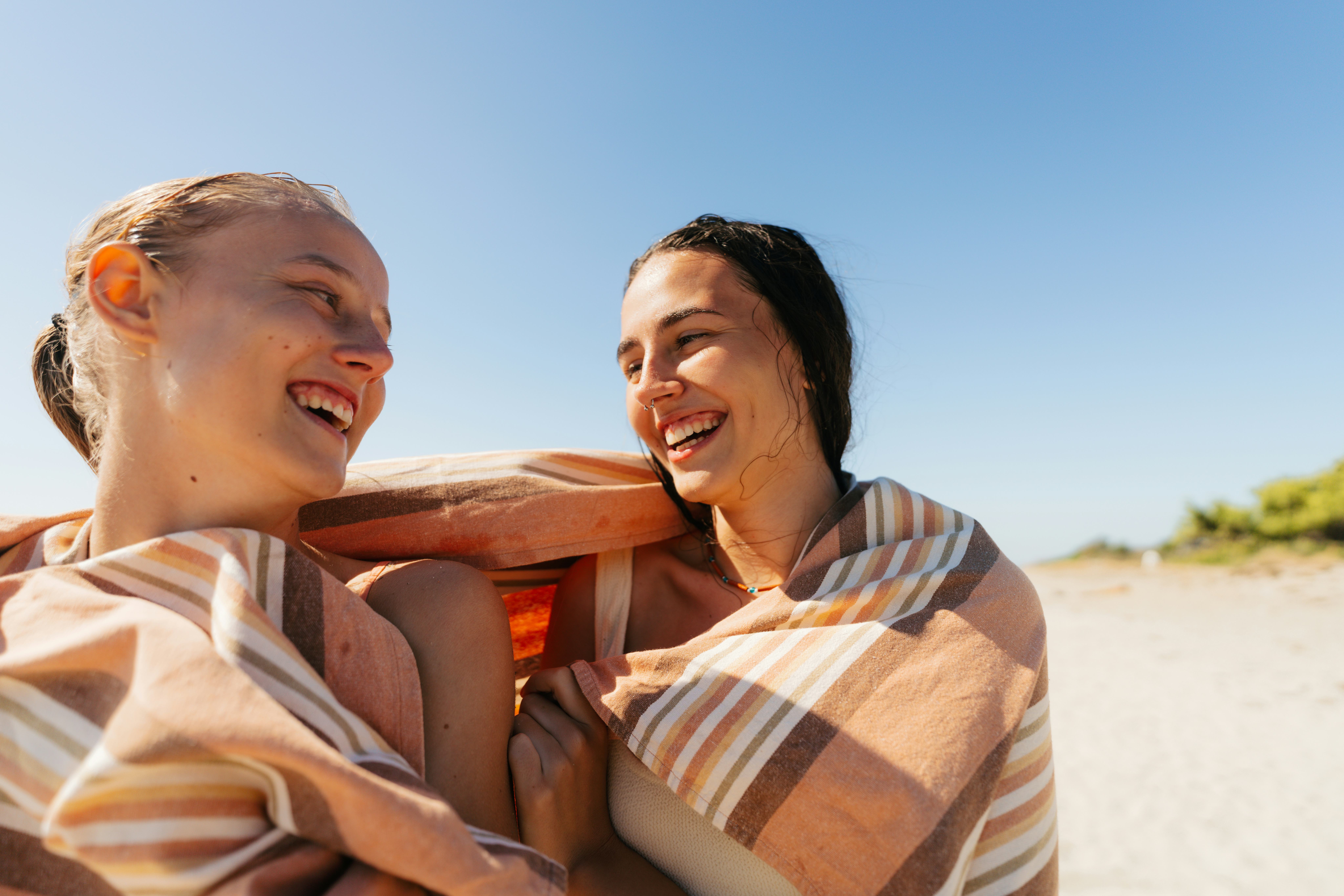 Two young friends wrapped in a towel on the beach making good jokes about summer and laughing.