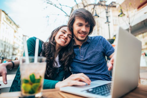 Happy young couple using laptop outdoor in sidewalk cafe. Cheerful man and woman on date sitting on ...