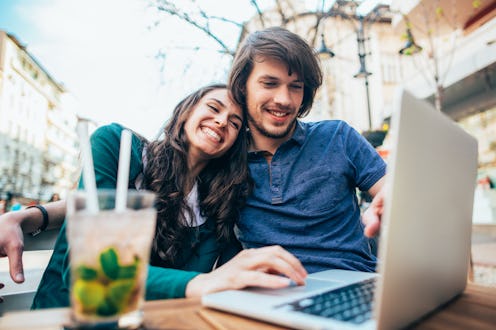 Happy young couple using laptop outdoor in sidewalk cafe. Cheerful man and woman on date sitting on ...