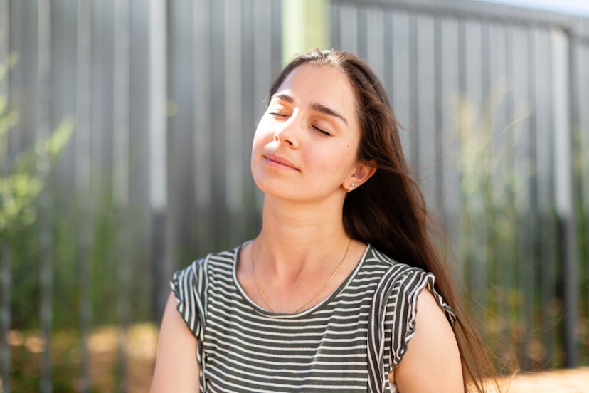 Young woman with closed eyes feeling relaxed and enjoying sunlight outside