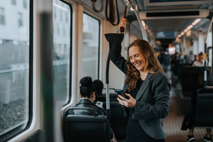 Woman standing on a train and laughing at good jokes about public transportation on her phone.