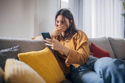 Young woman using smart phone while sitting on sofa in living room at home.