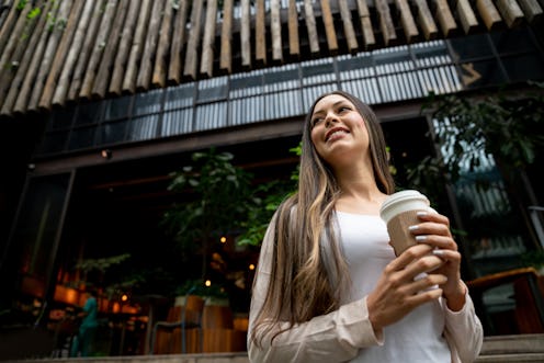 Portrait of beautiful latin american young woman leaving a coffee shop with a take out coffee lookin...