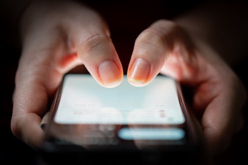 Close-up of two woman's thumbs touching on a smartphone screen in the dark.