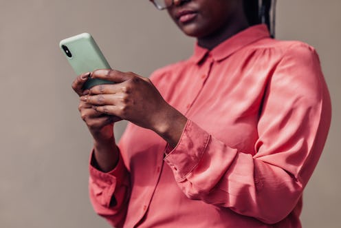 Close-up of an African American woman focused on her smartphone, wearing a fashionable pink blouse. ...