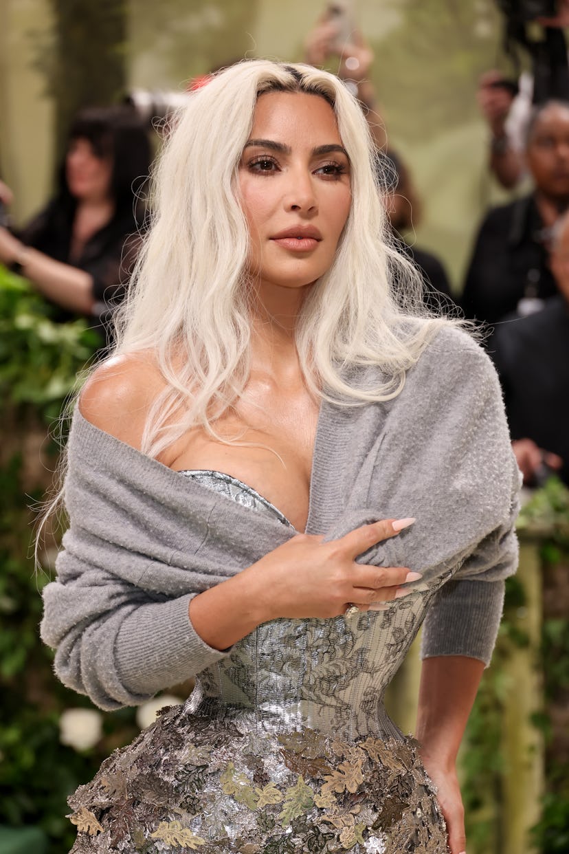 Kim Kardashian attends The 2024 Met Gala in a silver leaf dress and gray cardigan potentially belong...