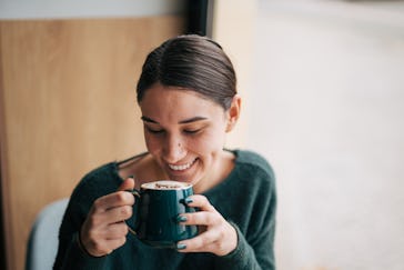 Close-up picture of a young smiling girl sitting in a coffee bar and enjoying a coffee.