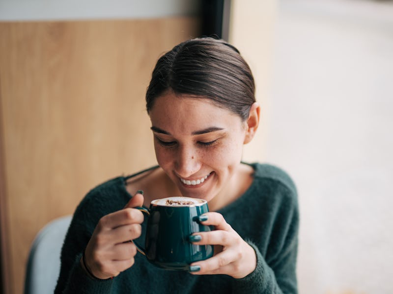 Close-up picture of a young smiling girl sitting in a coffee bar and enjoying a coffee.