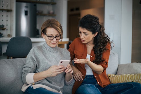 Young woman is arguing with her mother. They are sitting on sofa with legs crossed and senior woman ...