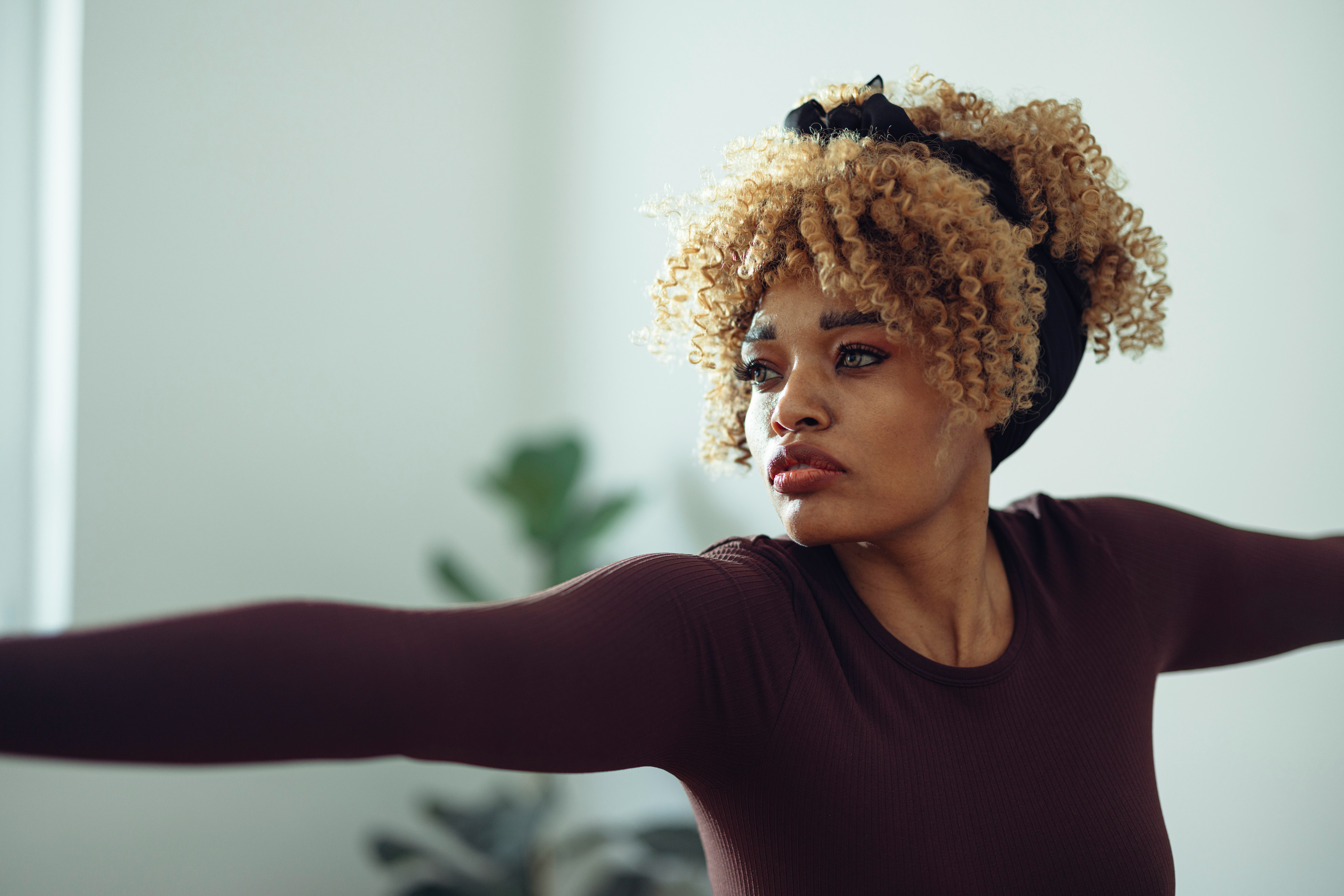 A woman doing a warrior yoga pose and listening to positive vibes quotes in her living room