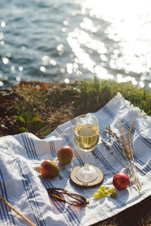 Summer picnic by sea. White blanket, summer fruits, glass of white wine, blurred blue sea water back...