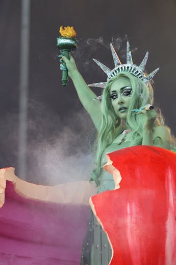 Performer dressed as a fantasy version of the Statue of Liberty, holding a torch, against a smoke-fi...