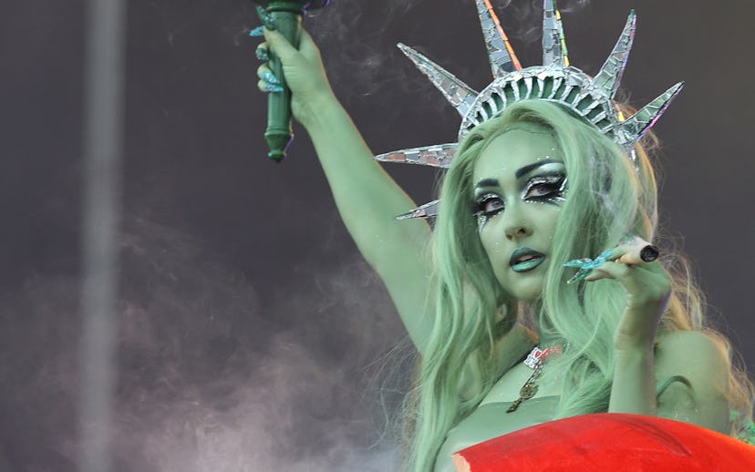 Performer dressed as a fantasy version of the Statue of Liberty, holding a torch, against a smoke-fi...