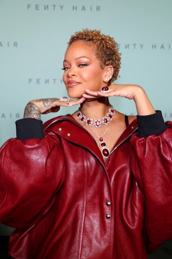 A woman in a large red leather jacket poses playfully at a Fenty Hair event, showcasing a detailed r...