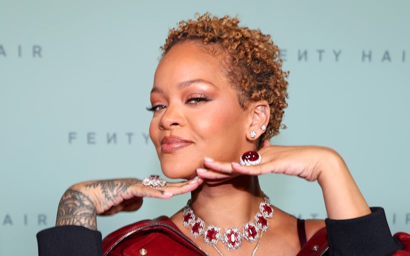 A woman in a large red leather jacket poses playfully at a Fenty Hair event, showcasing a detailed r...