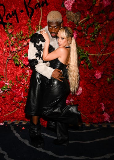 Two people stylishly dressed in leather pose against a vibrant floral backdrop at a Ray-Ban event.