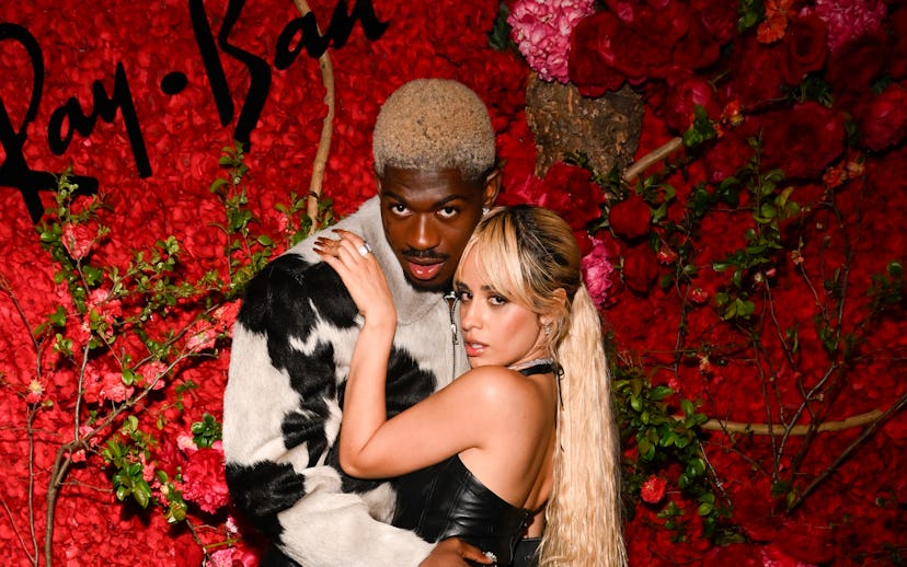 Two people stylishly dressed in leather pose against a vibrant floral backdrop at a Ray-Ban event.
