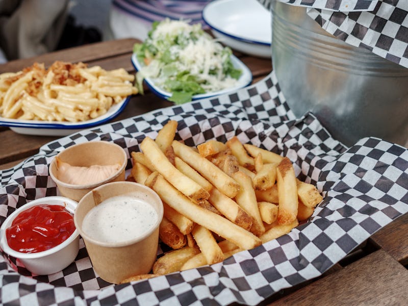 A close-up shot of a serving of golden, crispy French fries presented on a checkered paper. Accompan...