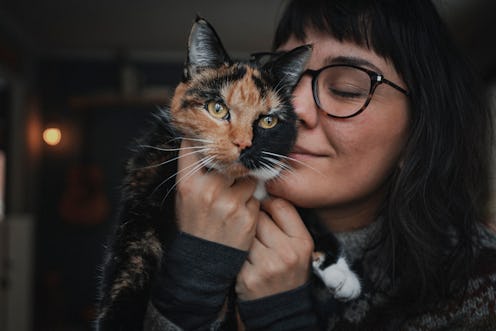 A close up of a young woman wearing glasses snuggling her brown and black cat with a unique name