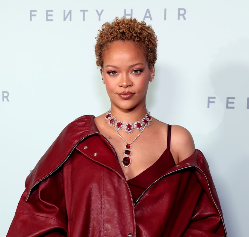 A woman in a burgundy leather jacket and a jewel necklace, standing in front of a Fenty Hair backdro...
